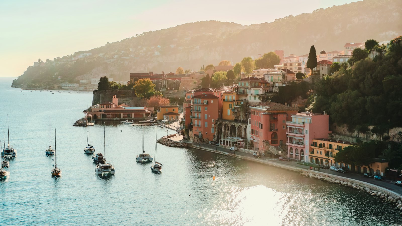 Baie de la Côte d’Azur au coucher du soleil, voiliers et maisons colorées au pied de la colline